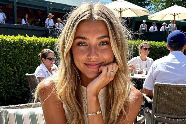 Portrait of a smiling blonde woman resting her chin on her hand at an outdoor restaurant table.