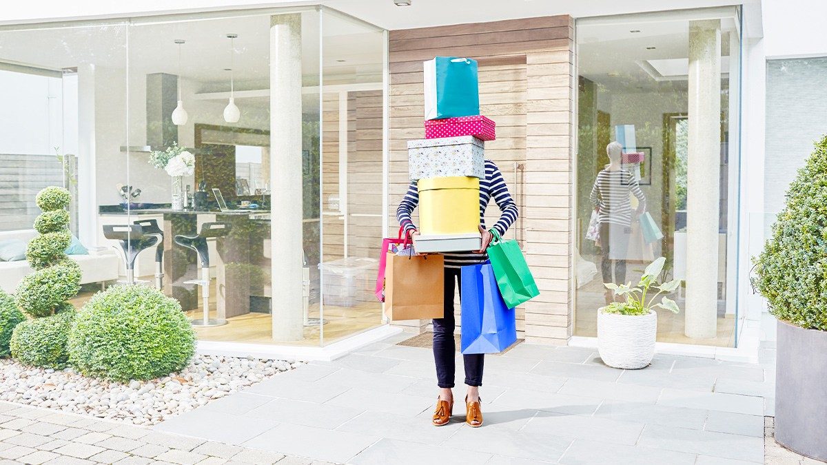 A shopper leaving a house carrying a tall stack of gift boxes and shopping bags.