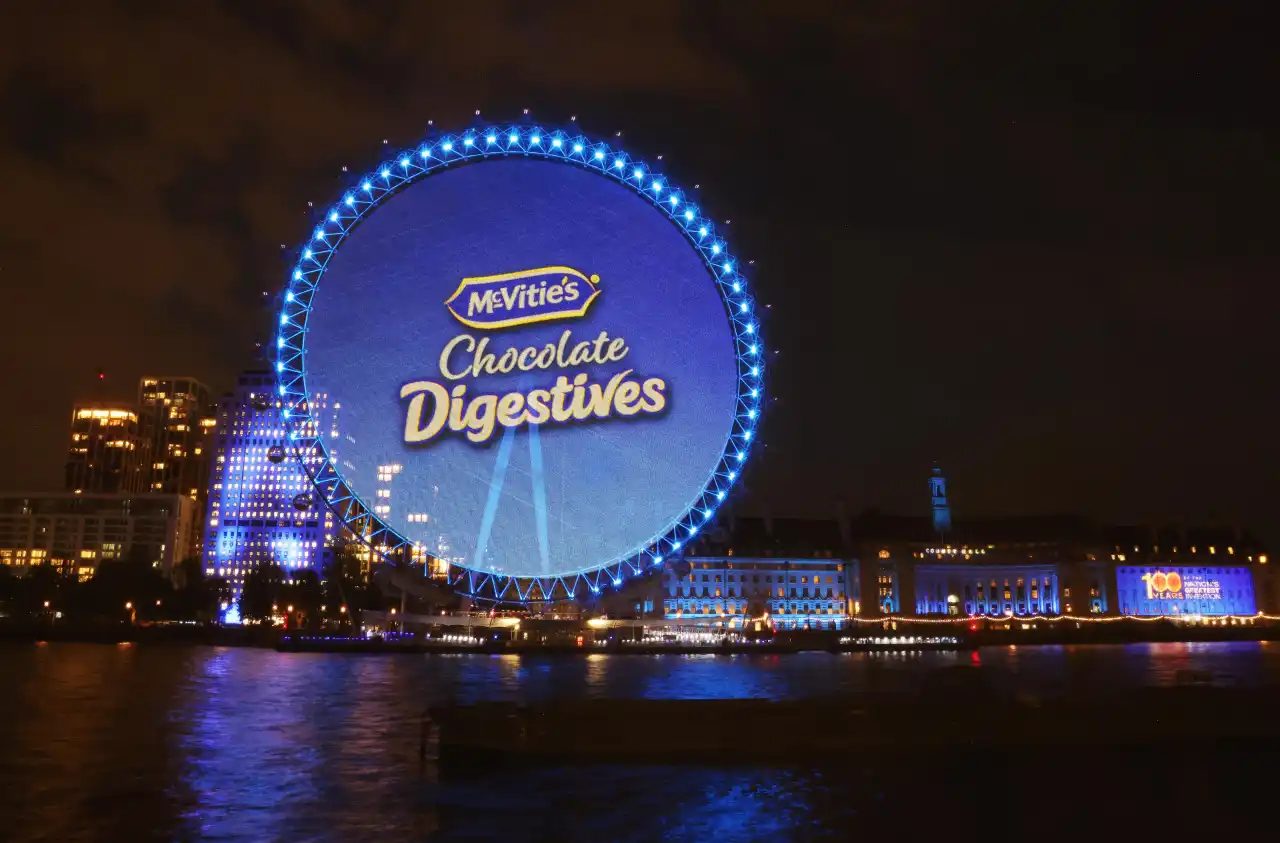 The London Eye lit up at night as a giant McVitie’s Chocolate Digestives biscuit, reflected in the Thames.
