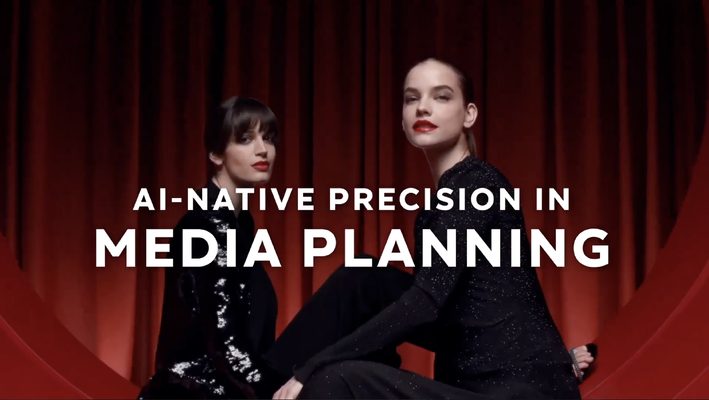 Video still of two models seated against a red curtain, captioned “AI-native precision in media planning”.